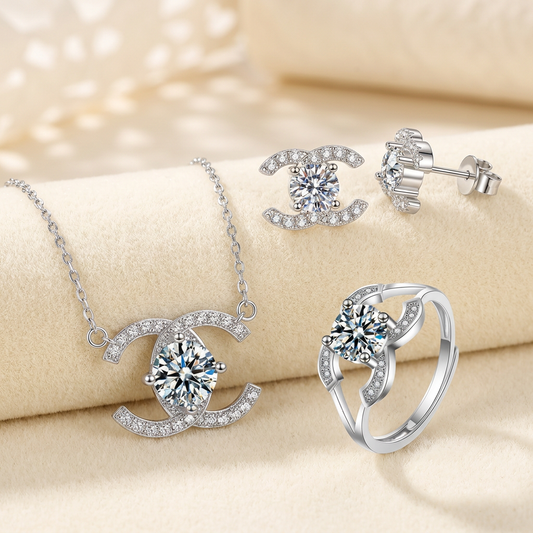Celeste sterling silver double-C moissanite necklace, pair of stud earrings and open ring on a cream display